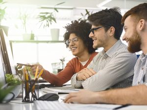 Three people at a desk in front of a monitor